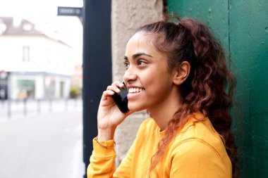 Şehirde cep telefonu ile konuşan gülümseyen genç kadının yakın profil portresi