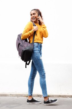 Cep telefonu ve çanta ile beyaz duvar tarafından gülümseyen güzel genç hintli kadının tam vücut yan portre