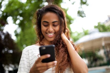 Gülümseyen ve cep telefonuna bakan güzel genç hintli kadının yakın portresi 