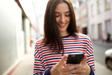 Şehirde cep telefonu bakarak gülümseyen genç kadın portresi