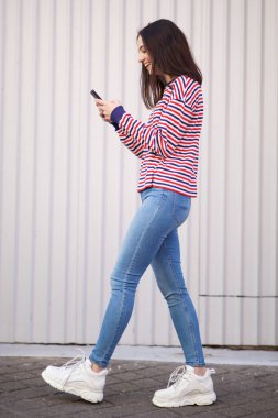 Cep telefonu ile yürüyen mutlu genç kadının tam vücut yan portre