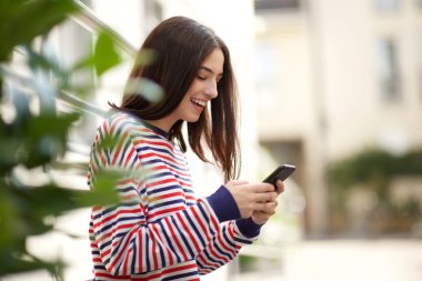 Dışarıda cep telefonu bakarak mutlu genç kadının yan portre