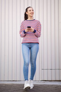 Cep telefonu ile yürüyen ve konuşan mutlu genç kadının tam uzunlukta portre