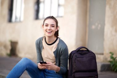 Cep telefonu ve çanta ile oturan mutlu kız öğrenci portresi