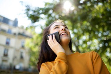 Parkta cep telefonu ile konuşan neşeli genç kadın portresi