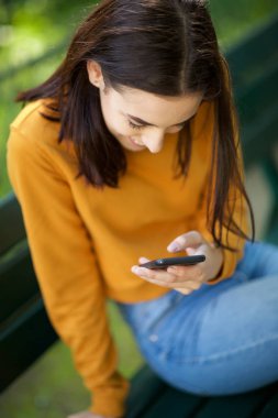 Parkta akıllı telefon bakarak mutlu genç kadının portresi