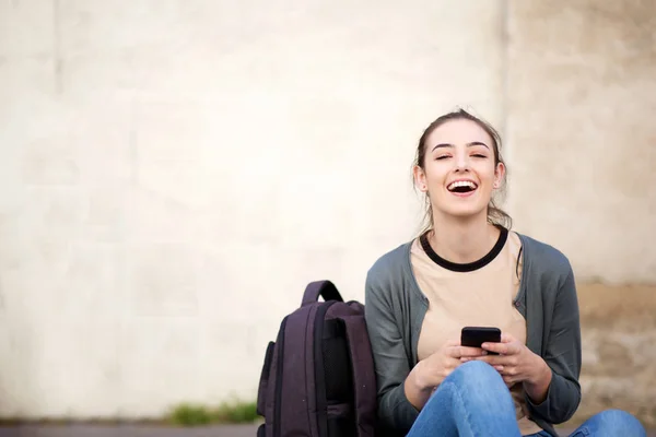 携帯電話で外に座っている笑う女子学生の肖像 — ストック写真