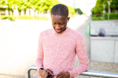 Genç siyah adam gülümseyen ve kulaklık ve cep telefonu ile müzik dinleme Portresi