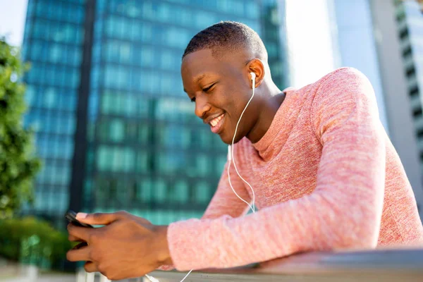 ヘッドフォンや携帯電話で音楽を聴く幸せな若い黒人男性のクローズアップ側の肖像画 — ストック写真