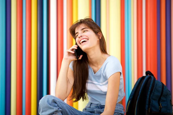 カラフルな壁に座って携帯電話で話し 笑う若い女性の肖像画 — ストック写真