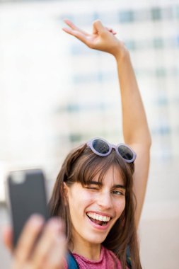 Tek kollu mutlu bir kadının portresi yakın çekimde cep telefonuyla selfie çekiyor.