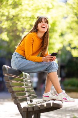 Parkta cep telefonuyla gülen mutlu bir kadının yan portresi