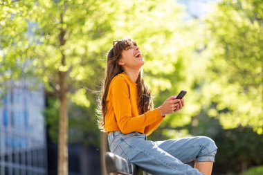 Parkta cep telefonuyla gülen mutlu bir kadının yan portresi