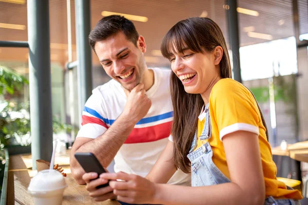 Kafede oturan ve cep telefonuna bakan sevgililer.