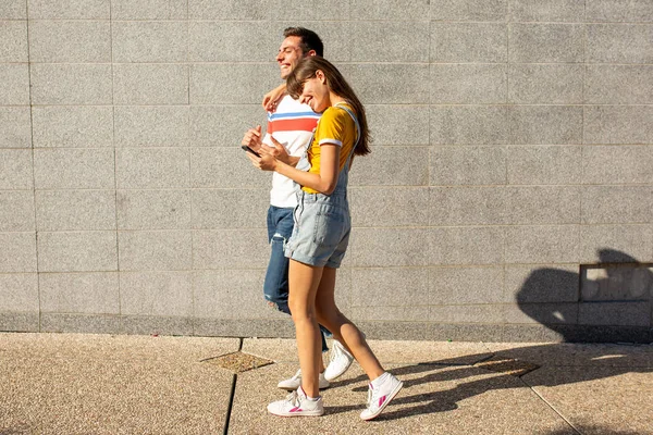 フルボディサイドポートレートのボーイフレンドとガールフレンド歩くとともに外で携帯電話 — ストック写真