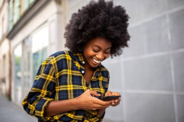 Sokakta yürüyen ve cep telefonuna bakan siyahi bir kadının portresi.