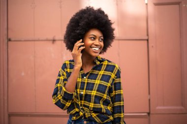 Mutlu gülümseyen genç zenci kadın portresi cep telefonuyla konuşuyor ve başka tarafa bakıyor.