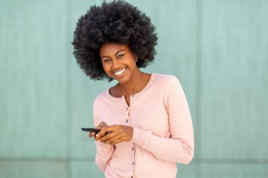 Yeşil duvarda cep telefonuyla gülümseyen Afro-Amerikan kadın portresini kapatın.