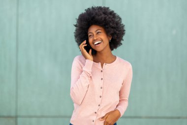 Yatay portreyi kapat. Afro-Amerikan kadın cep telefonuyla yeşil arka planda konuşuyor.