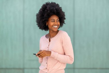 Cep telefonuyla gülümseyen ve yeşil duvardan bakan Afro-Amerikan kadın portresini kapat.