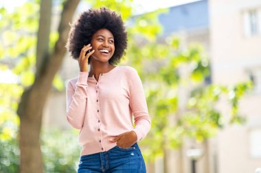 Dışarıda cep telefonuyla konuşan mutlu Afro-Amerikan kadının portresi.