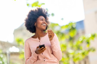 Dışarıda cep telefonuyla gülen Afrikalı Amerikalı genç bir kadının portresi.