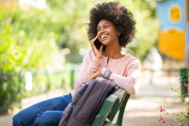 Parktaki bankta oturmuş cep telefonuyla konuşan gülümseyen zenci kadının portresi.