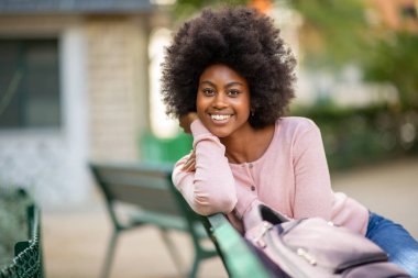 Afro saçlı güzel, Afro-Amerikan bir kadının park bankında otururken çekilmiş portresi.