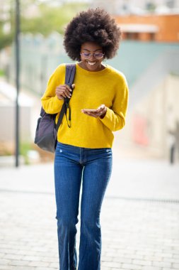 Gözlüklü, gülümseyen ve cep telefonuna bakan Afro-Amerikan kadının portresi.