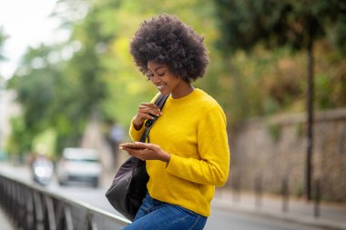 Dışarıda oturmuş cep telefonuna bakan genç bir kadının portresi.