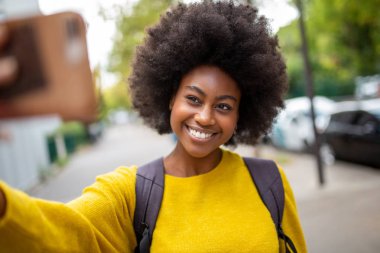 Dışarıda cep telefonuyla selfie çeken gülümseyen Afrikalı Amerikalı kadının portresi.