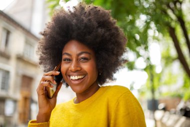 Çekici ve genç Afrikalı bir kadının portresi. Gülümsüyor ve dışarıda cep telefonuyla konuşuyor.