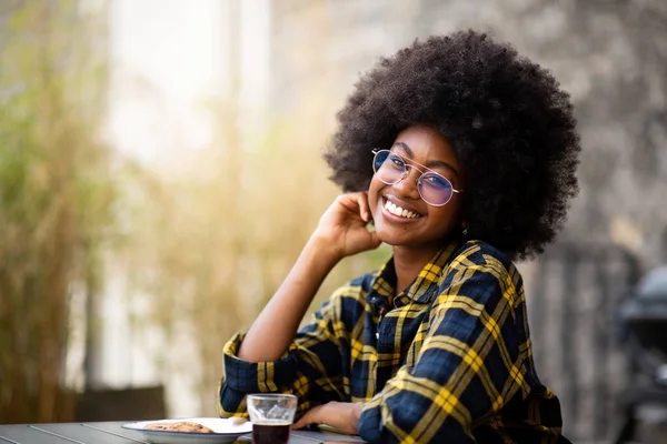 Portrait of young black woman with afro hair and glasses sitting outside and smiling