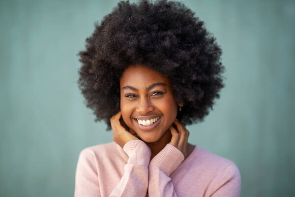 Close up front portrait of attractive young african american woman with afro smiling and hand on face