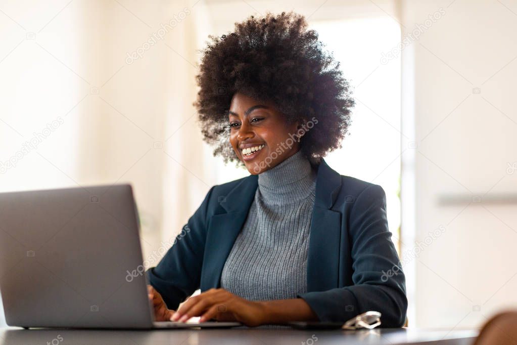 Portrait of young black businesswoman sitting in office smiling and looking at laptop