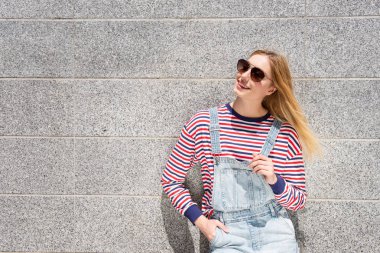 Duvarda gülümseyen güneş gözlüklü havalı sarışın kız portresi.