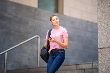Okulda çantalı ve cep telefonlu gülümseyen kız portresi.