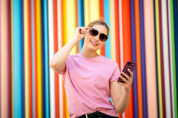 色彩艳丽的金发女孩手持手机和太阳镜的肖像 — 图库照片