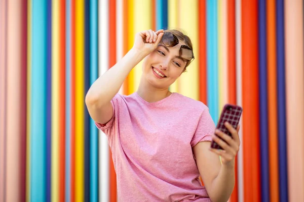 Portret Blondynki Trzymającej Telefon Komórkowy Okulary Przeciwsłoneczne Przy Kolorowych Ścianach — Zdjęcie stockowe