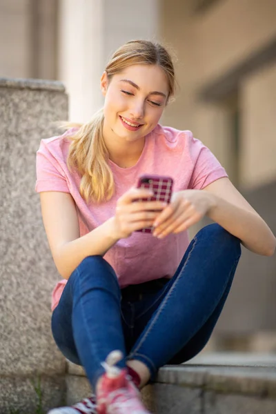 Портрет Улыбающейся Девочки Подростка Сидящей Снаружи Смотрящей Мобильный Телефон — стоковое фото