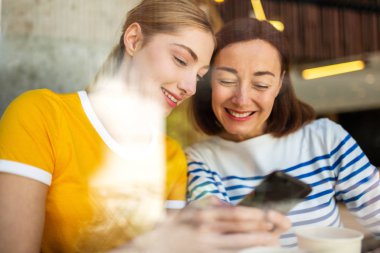 Kafede oturup cep telefonuna bakarak gülümseyen anne ve kızın portresi.