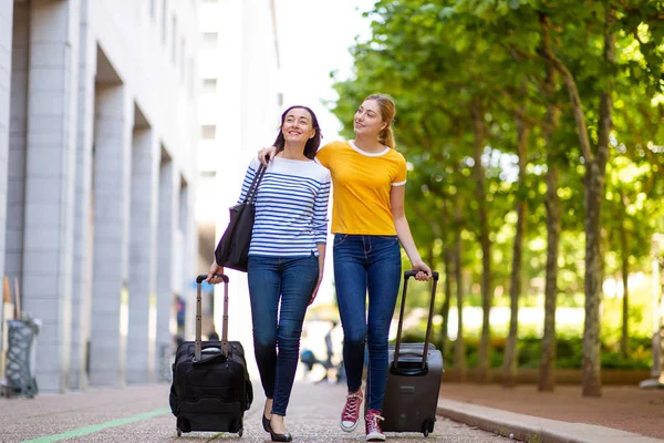 Full body portrait of happy mother and daughter walking outdoors with travel bags