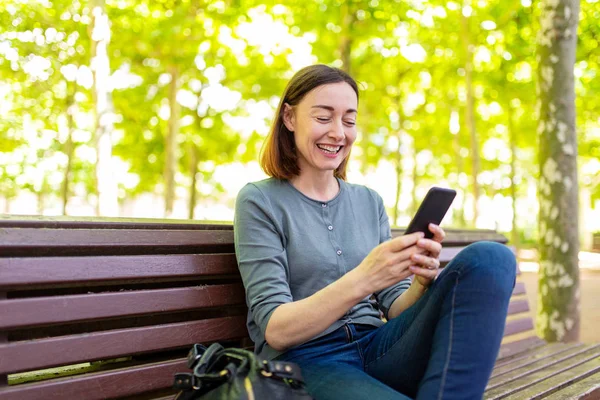 Retrato Sonriente Mujer Mediana Edad Sentada Parque Con Teléfono Móvil — Foto de Stock