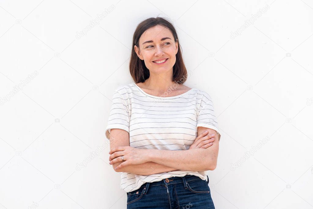 Portrait smiling older woman standing by white background with arms crossed and glancing