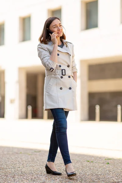 Full body portrait trendy older woman walking on street talking with mobile phone