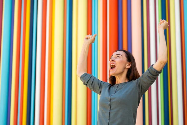 Portrait cheerful woman with arms raised by colorful background