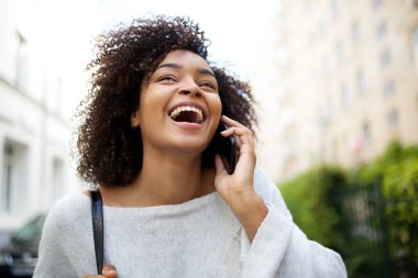 Dışarıda cep telefonuyla konuşan kıvırcık saçlı, mutlu, Afro-Amerikan kadının portresini yakından çek.