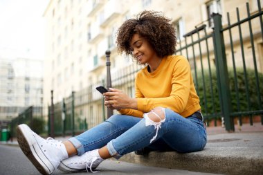 Sokakta cep telefonuyla oturan havalı Afro-Amerikan kadının portresi.