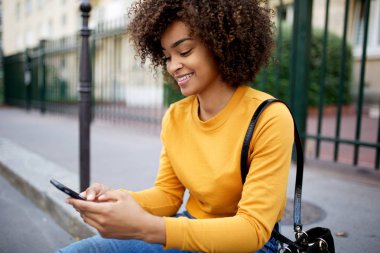 Şehirde cep telefonuna bakan gülümseyen Afrikalı Amerikalı kadının portresi.