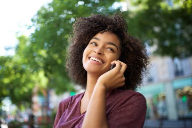 Dışarıda cep telefonuyla konuşan gülümseyen Afro-Amerikan kadın portresi.